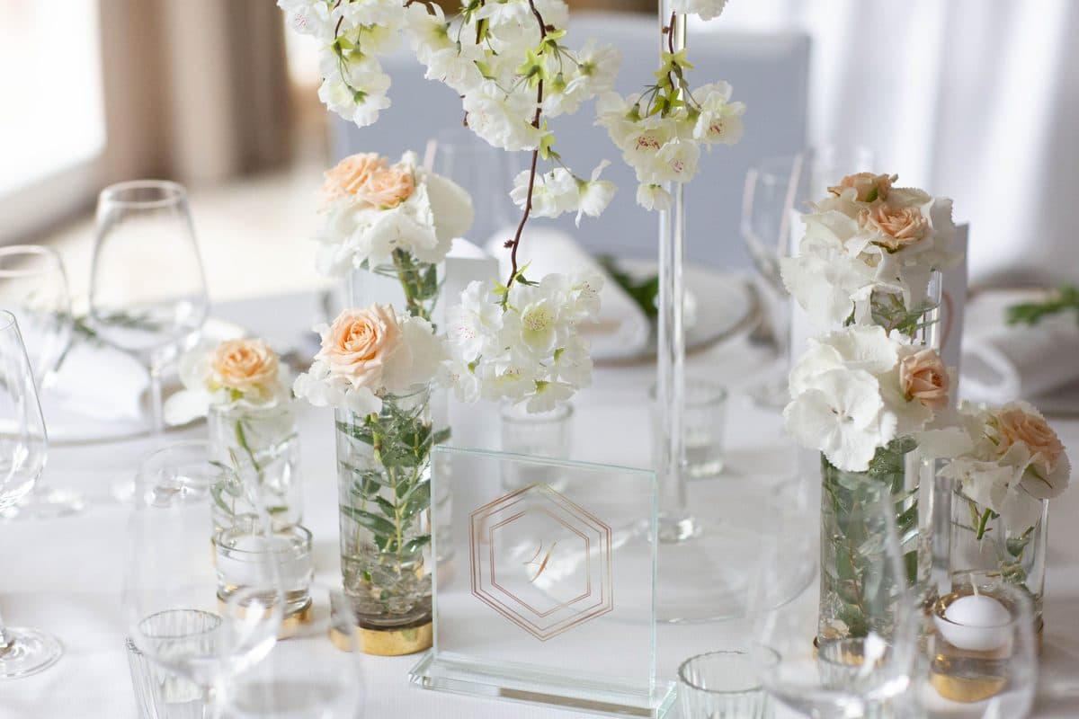 Tischdeko-Detail mit weißem Kirschblütenzweig, Minizylinder-Vasen mit Rosen und Hortensien sowie Kristall-Tischnummer