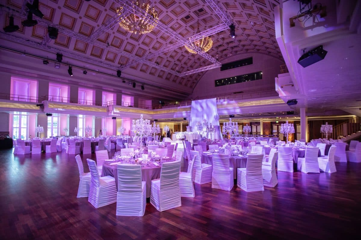 Bénazetsaal im Kurhaus Baden-Baden mit goldener Kassettendecke, Kristall-Kronleuchtern und runden Hochzeitstischen bei lila Eventbeleuchtung