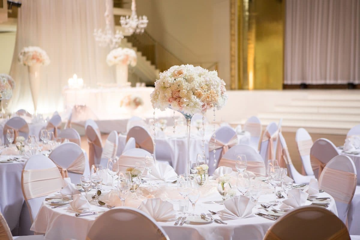 Hochzeitstisch im Bénazetsaal mit hohem Blumengesteck auf Martiniglas-Vase, herabhängenden Kristallanhängern und gefächerten Servietten