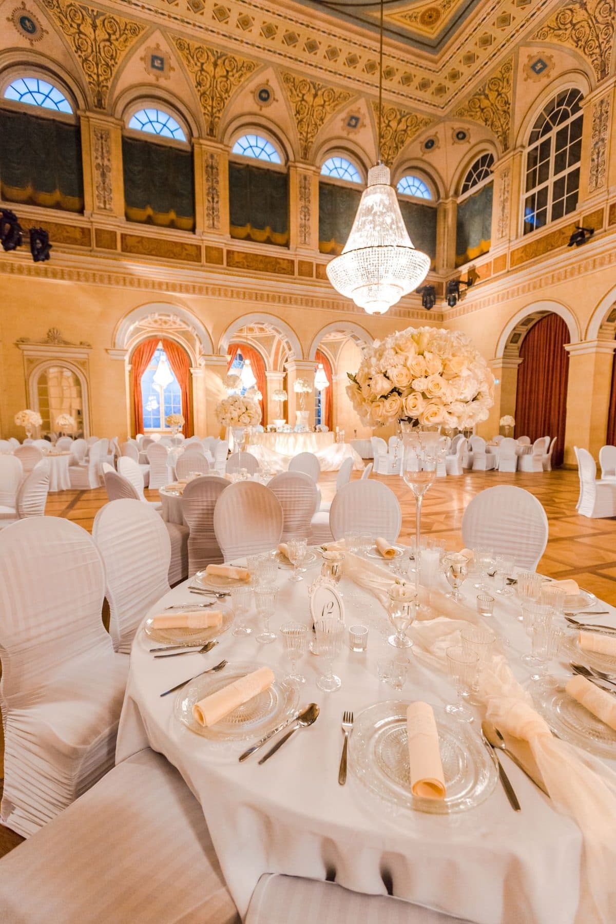 Hochzeitstisch im König Ludwig I.-Saal mit hohem Rosengesteck, Kristallgläsern und Blick auf den historischen Festsaal