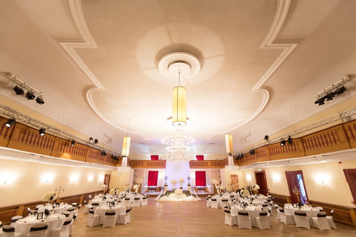 Redoutensaal Erlangen mit historischer Holzgalerie, Kristallkronleuchtern und runden Hochzeitstischen in Schwarz-Weiß