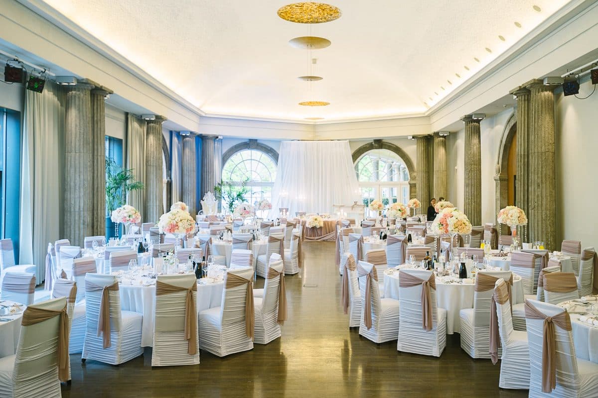 Kursaal der Trinkkuranlage Bad Nauheim mit Säulen, Rundbogenfenstern und runden Hochzeitstischen mit altrosa Stuhlschleifen