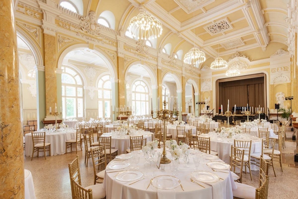 Elegante Hochzeitstische mit weißen Blumengestecken und goldenen Kerzenhaltern