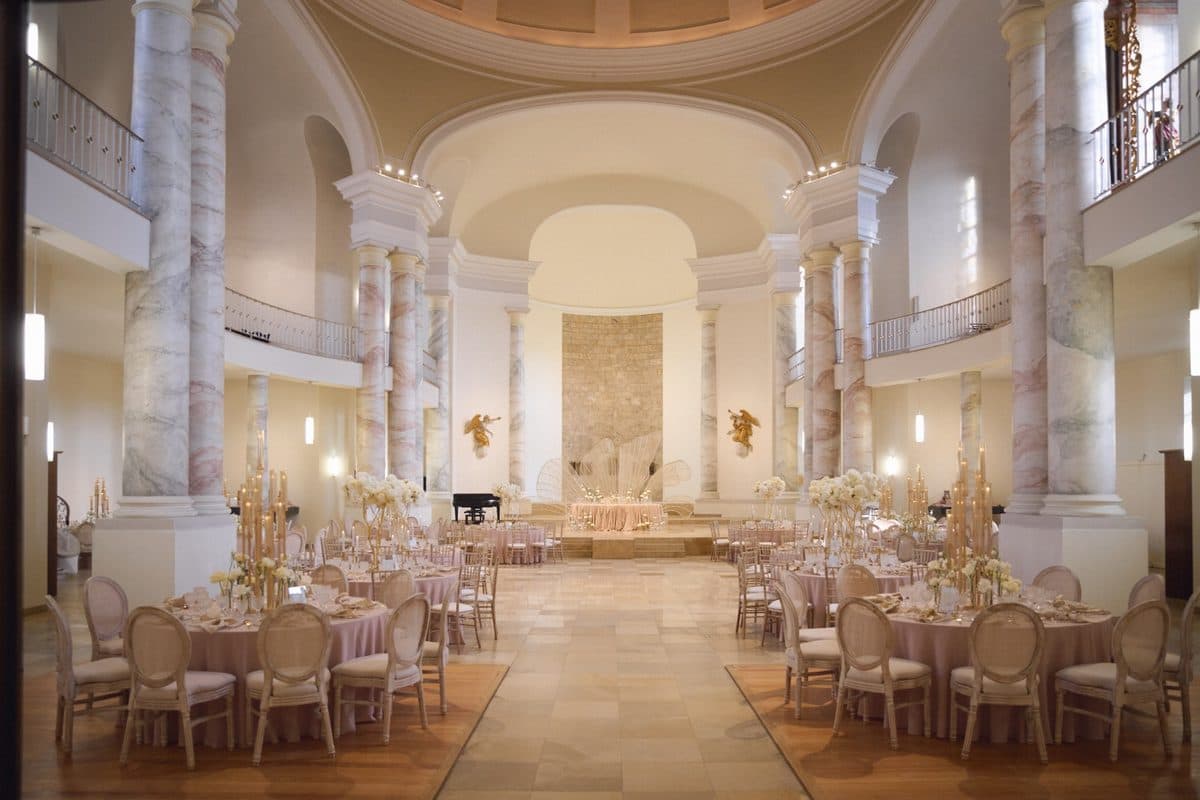 Festsaal mit Marmorsäulen, rosafarbenen Tischdecken und hohen goldenen Kerzenständern