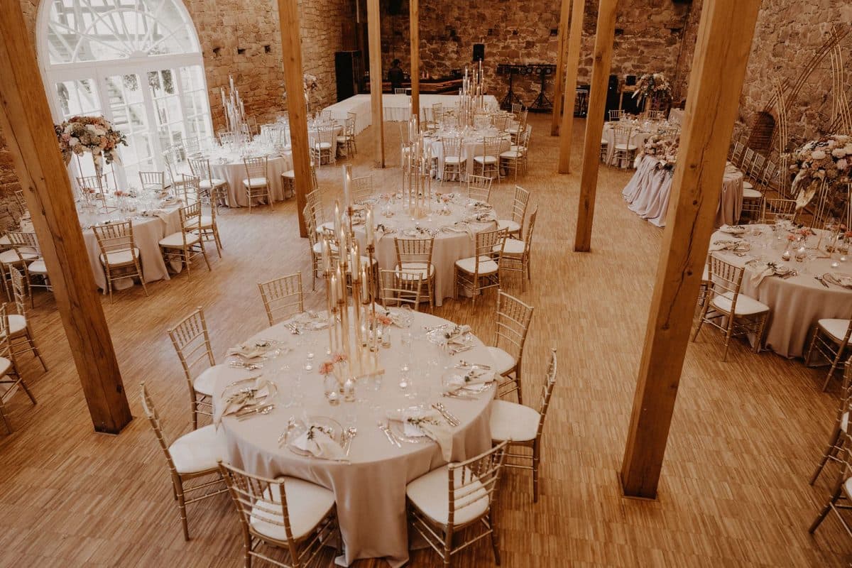 Rustikaler Scheunensaal mit Holzbalken, Natursteinwänden und runden Hochzeitstischen