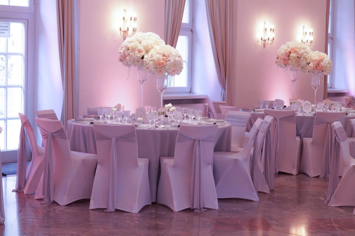 Festlich gedeckte Hochzeitstische mit rosa Stuhlhussen und hohen Blumengestecken