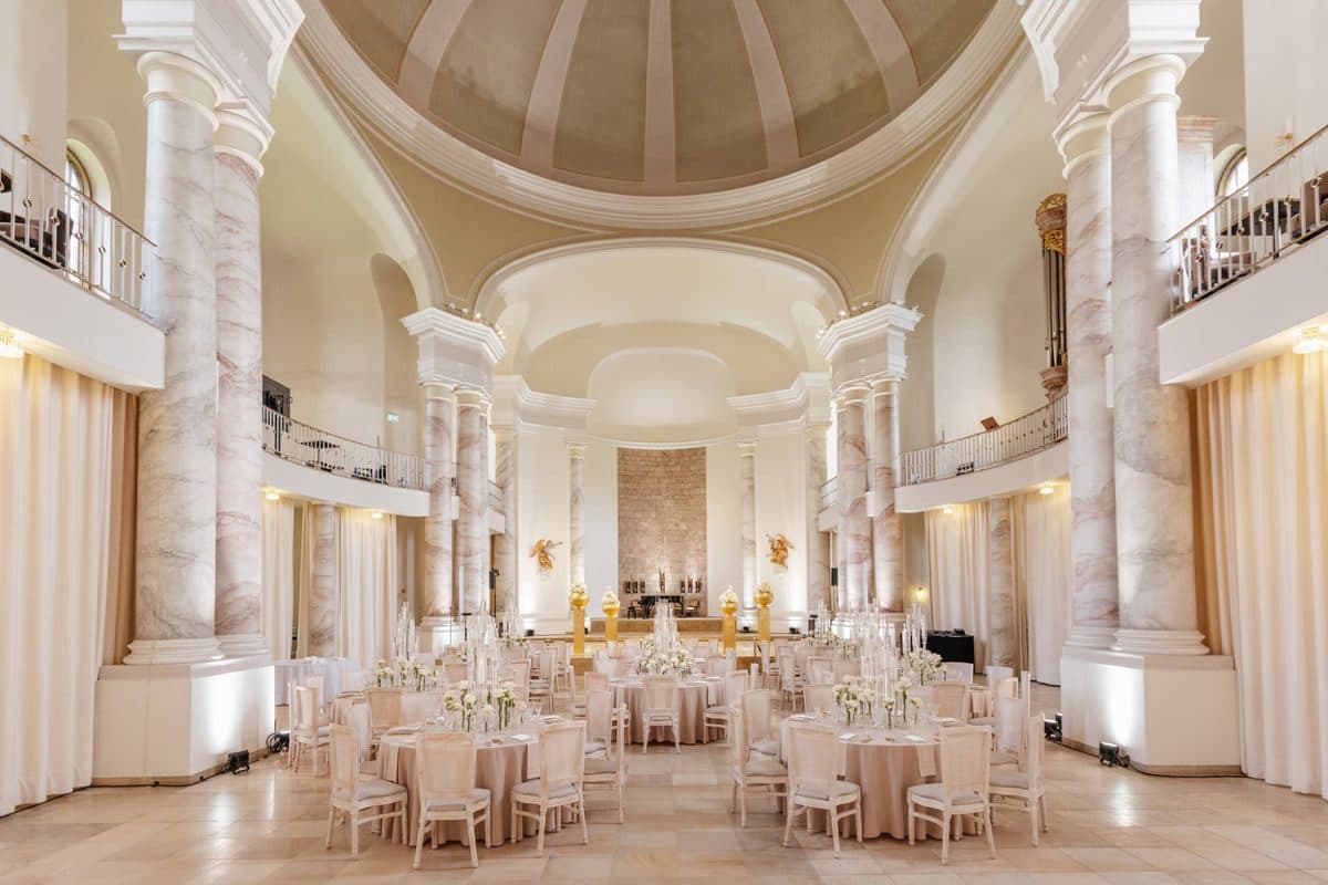 Kuppelsaal mit Marmorsäulen, Balkonen und runden Hochzeitstischen in Champagner
