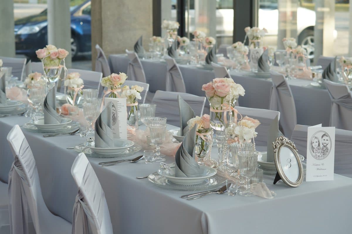 Detailaufnahme gedeckter Tafel mit grauen Servietten, rosa Rosen und silbernem Besteck