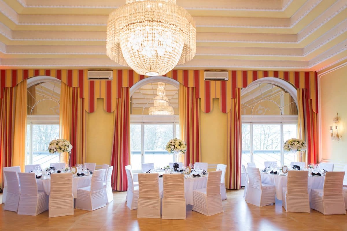 Festsaal mit gestreiften Vorhängen, Kristall-Kronleuchtern und weißen Rosen-Gestecken