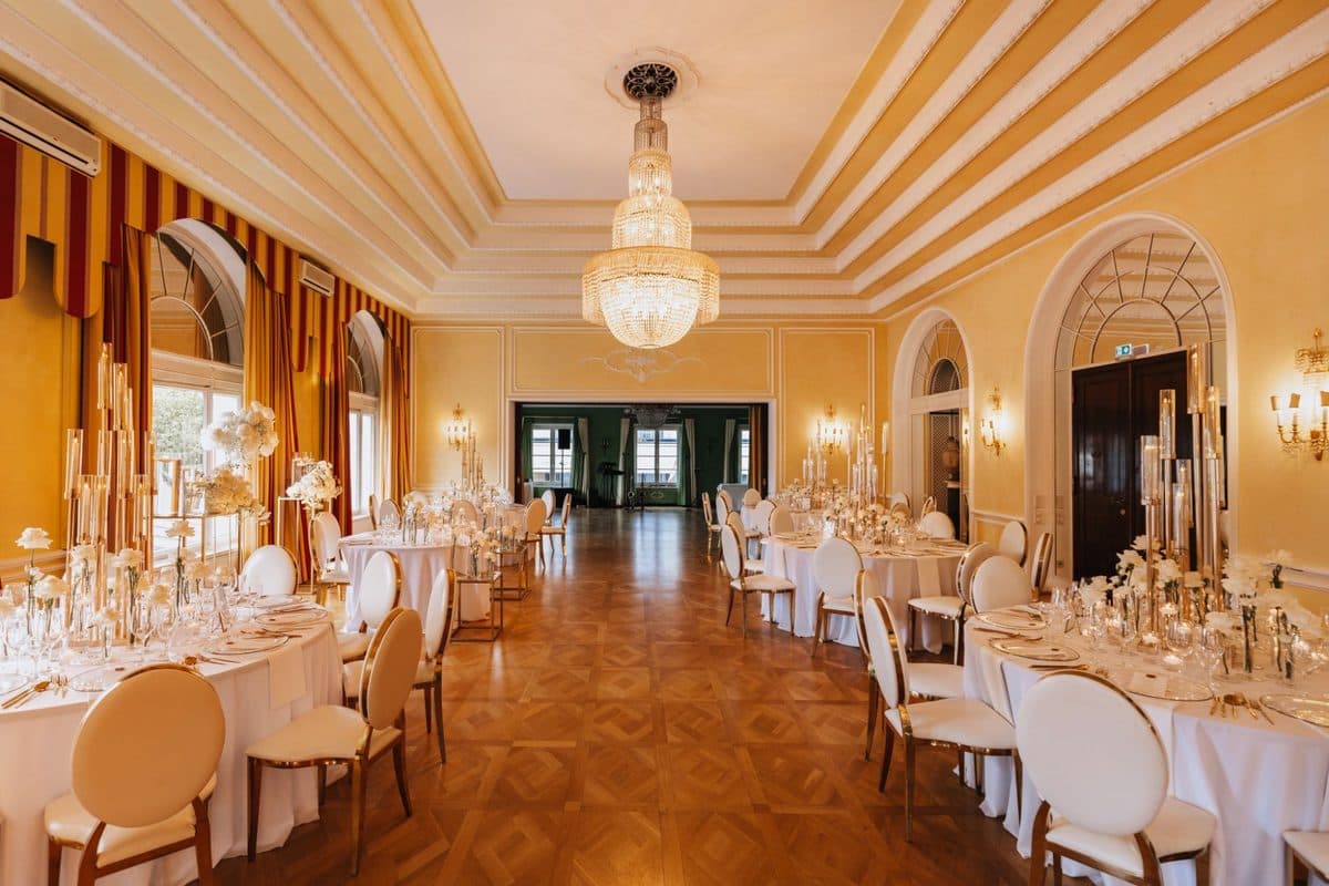 Festsaal mit gestreiften Vorhängen, Kristall-Kronleuchter und goldenen Kerzensäulen mit weißen Rosen