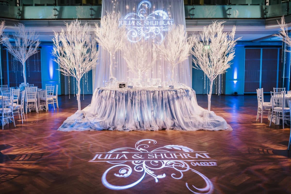 Brauttisch mit weißen Winterbäumen, Kristallvorhang und Namens-Gobo auf dem Tanzboden