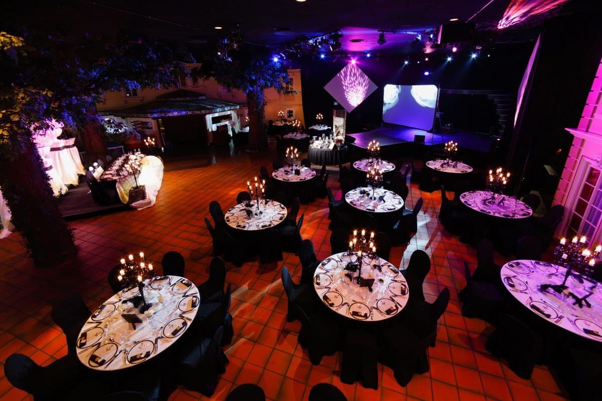Festsaal mit Baum-Deko, runden Tischen in Schwarz-Weiß und Bühne mit Lichtshow