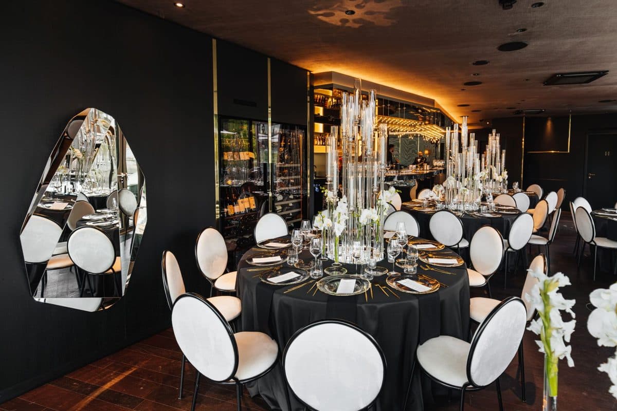 Festlich gedeckte Tafel in Schwarz mit hohen Glas-Kerzensäulen und weißen Orchideen in edler Bar-Lounge