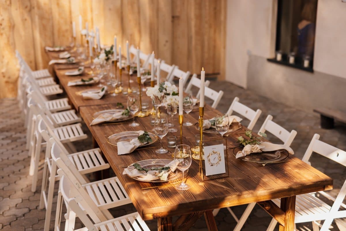 Lange festlich gedeckte Hochzeitstafel unter Holzpavillon im warmen Abendlicht mit goldenen Kerzenleuchtern und weißen Blumen