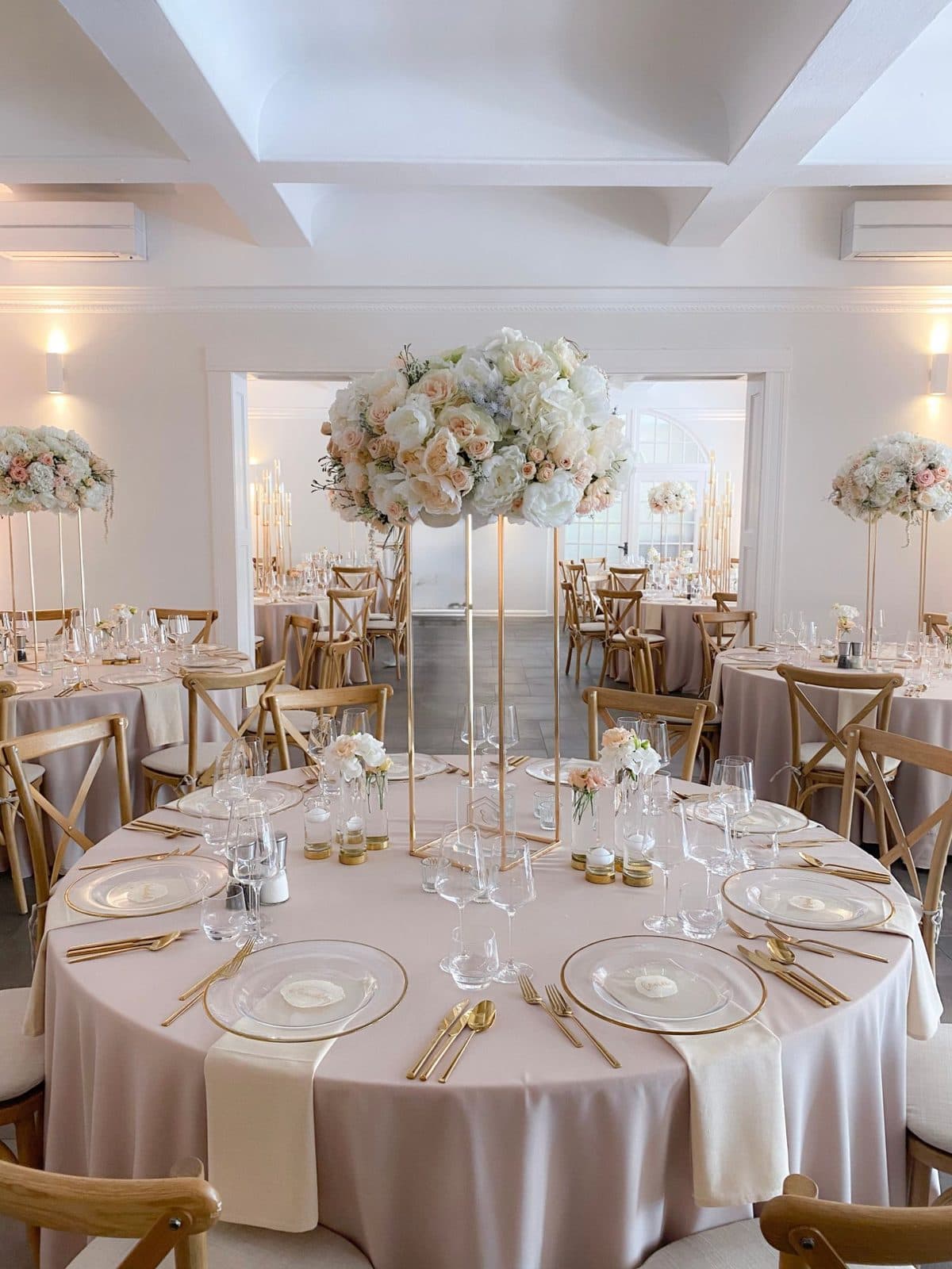 Runder Hochzeitstisch mit hoher weiß-rosé Blumenkugel auf goldenem Ständer, transparenten Glastellern und goldenem Besteck